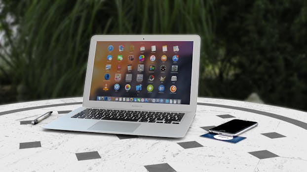 Open laptop with app icons displayed, smartphone and pen on white table outdoors.